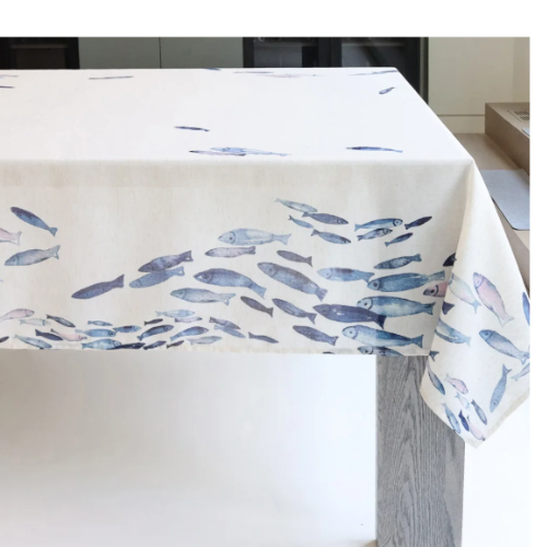 White linen-blend tablecloth with watercolour blue fish print on a dining table / Nappe en mélange de lin blanc avec imprimé de poissons bleus aquarellés sur une table à manger