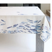 White linen-blend tablecloth with watercolour blue fish print on a dining table / Nappe en mélange de lin blanc avec imprimé de poissons bleus aquarellés sur une table à manger