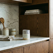 Kitchen counter with ceramic containers, wooden spoons, and books on a marble backsplash.