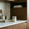 Kitchen counter with ceramic containers, wooden spoons, and books on a marble backsplash.
