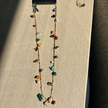 Gold-plated semi-precious stone charm necklace displayed on wood block, colorful stones including amethyst and turquoise — Reyca / Collier charm plaqué or avec pierres semi-précieuses exposé sur bloc de bois, pierres colorées dont améthyste et turquoise — Reyca