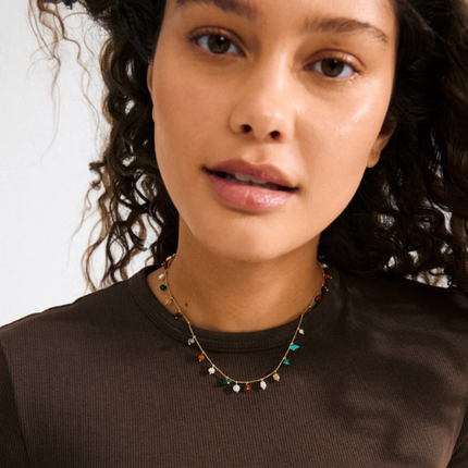Gold semi-precious stone charm necklace worn on model with dark curly hair and brown top — Reyca / Collier charm plaqué or avec pierres semi-précieuses porté par un mannequin aux cheveux bouclés foncés et haut brun — Reyca