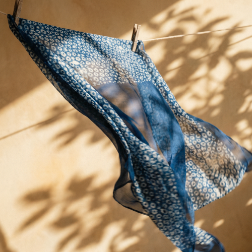 Hand block-printed indigo cotton scarf laid flat on a wooden surface, showing solid navy half and white oval block-print pattern half.