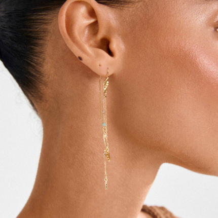 Close-up side view of model wearing gold plated asymmetric drop earrings with delicate chains and colourful beads | Vue latérale rapprochée de boucles d'oreilles pendantes asymétriques plaquées or avec chaînes délicates et perles colorées