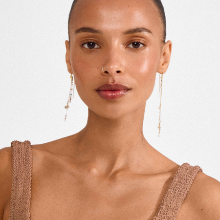 Model wearing gold plated asymmetric charm drop earrings with chains, sun charm and starfish | Modèle portant des boucles d'oreilles pendantes asymétriques plaquées or avec chaînes, charm soleil et étoile de mer