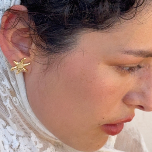 Boucle d'oreille clou étoile de mer dorée portée sur le lobe d'un modèle aux cheveux foncés — Reyca