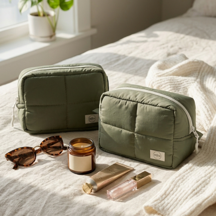Two green toiletry bags on a bed with sunglasses and skincare products.