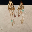 Close-up of gold triple hoop drop earrings with colorful glass bead charms on stone surface — Reyca / Gros plan de boucles d'oreilles triple anneau doré avec charms en perles de verre colorées sur surface en pierre — Reyca