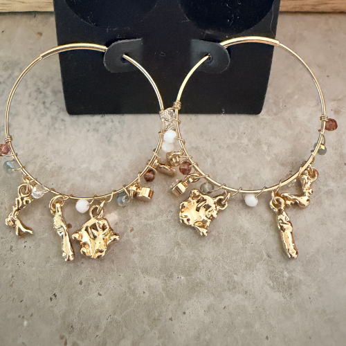 Close-up of gold hoop earrings with sculptural charms on packaging showing glass beads detail — Reyca / Gros plan de boucles d'oreilles créoles dorées avec charms sculptés sur emballage, détail des perles de verre — Reyca
